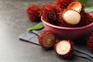 Photo of Delicious ripe rambutans and green leaves on grey table, closeup. Space for text