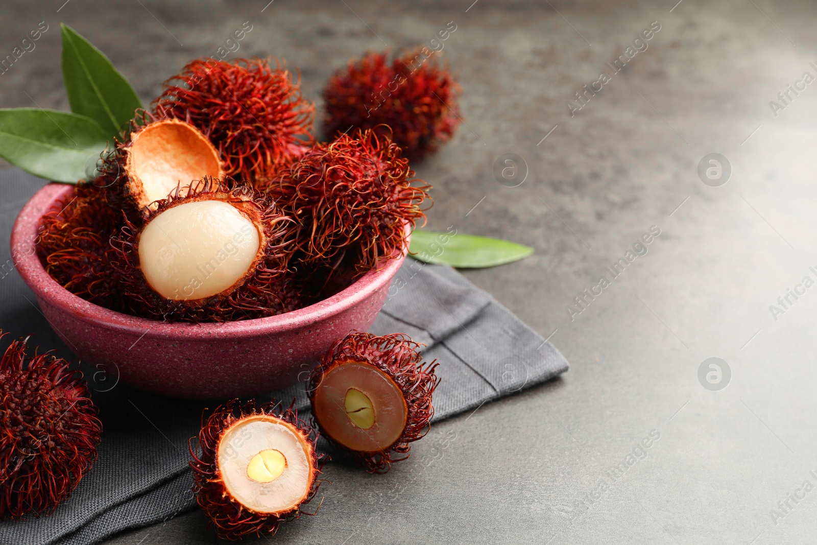 Photo of Delicious ripe rambutans and green leaves on grey table, closeup. Space for text