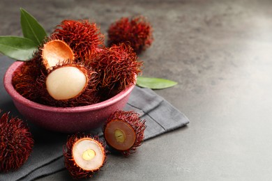 Photo of Delicious ripe rambutans and green leaves on grey table, closeup. Space for text