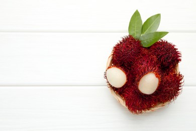 Photo of Delicious ripe rambutans and green leaves on white wooden table, top view. Space for text