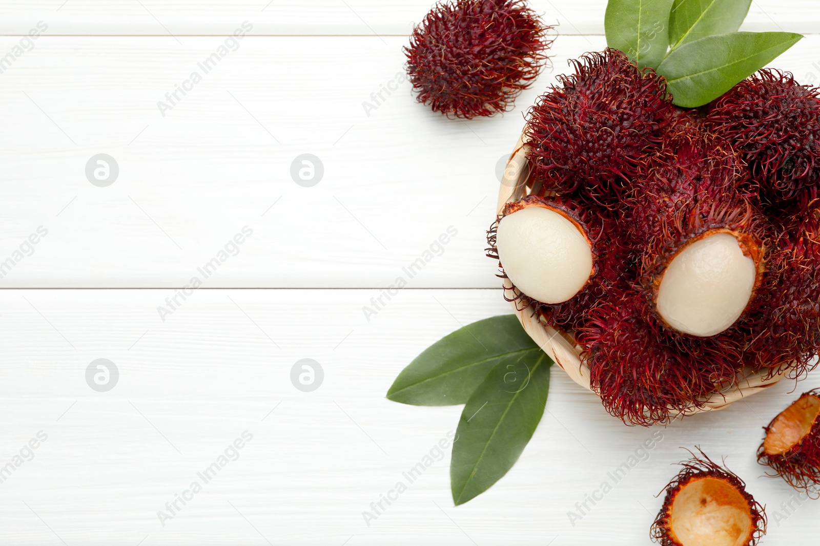 Photo of Delicious ripe rambutans and green leaves on white wooden table, top view. Space for text