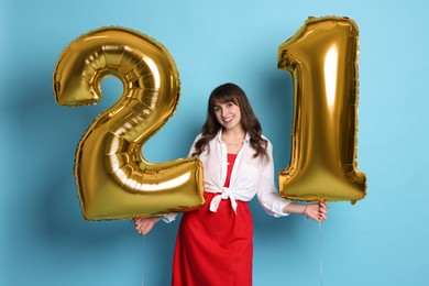 Photo of Coming of age party - 21st birthday. Young woman holding number shaped balloons on light blue background