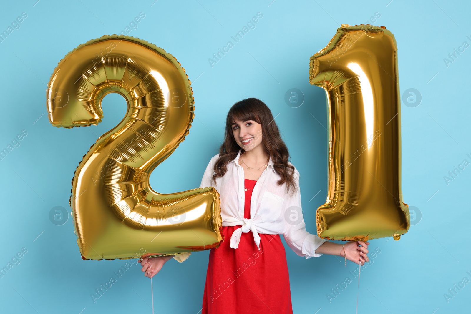 Photo of Coming of age party - 21st birthday. Young woman holding number shaped balloons on light blue background