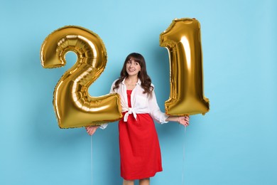 Photo of Coming of age party - 21st birthday. Young woman holding number shaped balloons on light blue background