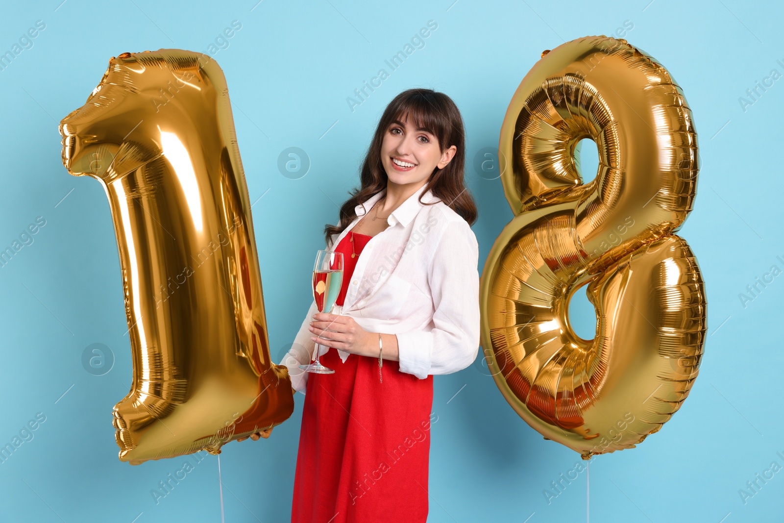 Photo of Coming of age party - 18th birthday. Young woman with glass of wine holding number shaped balloons on light blue background