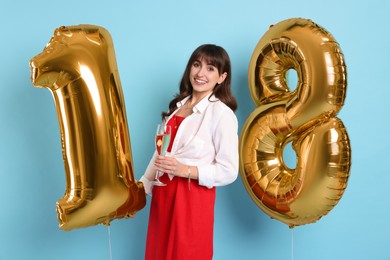 Photo of Coming of age party - 18th birthday. Young woman with glass of wine holding number shaped balloons on light blue background