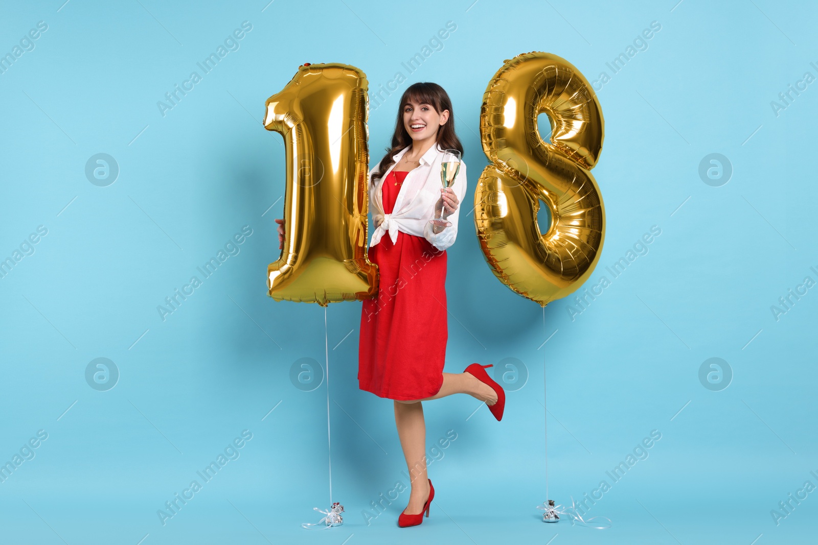 Photo of Coming of age party - 18th birthday. Young woman with glass of wine holding number shaped balloons on light blue background