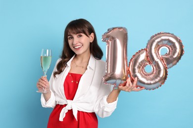 Photo of Coming of age party - 18th birthday. Young woman with glass of wine holding number shaped balloons on light blue background