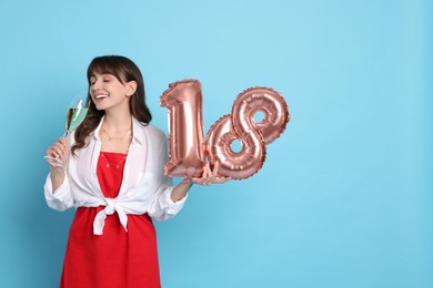 Coming of age party - 18th birthday. Young woman with glass of wine holding number shaped balloons on light blue background, space for text