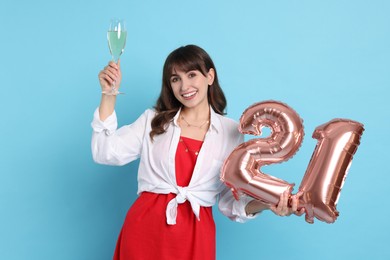 Coming of age party - 21st birthday. Young woman with glass of wine holding number shaped balloons on light blue background