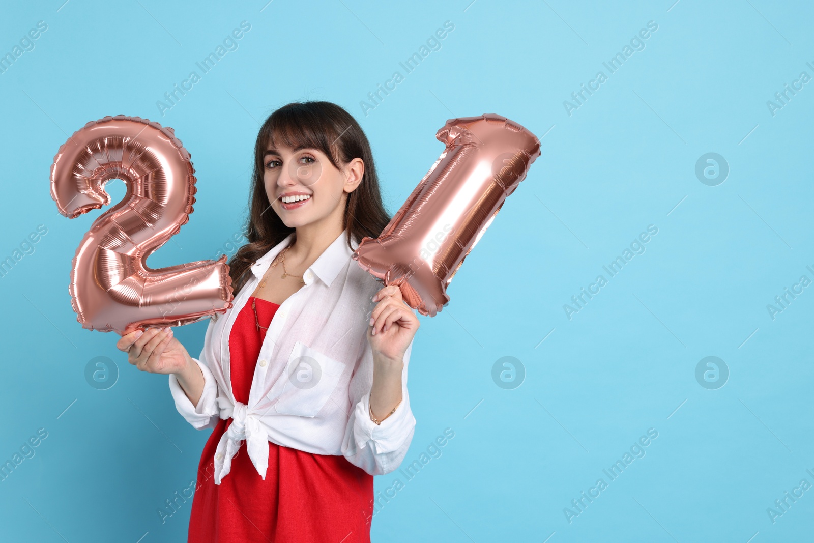 Photo of Coming of age party - 21st birthday. Young woman holding number shaped balloons on light blue background, space for text