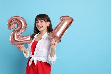 Coming of age party - 21st birthday. Young woman holding number shaped balloons on light blue background, space for text