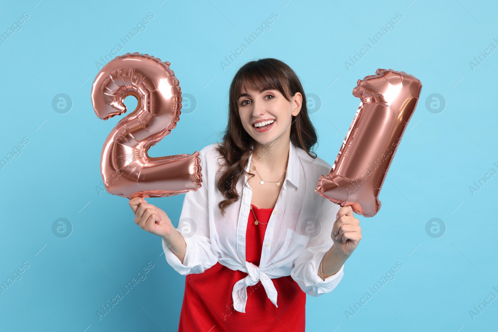 Photo of Coming of age party - 21st birthday. Young woman holding number shaped balloons on light blue background