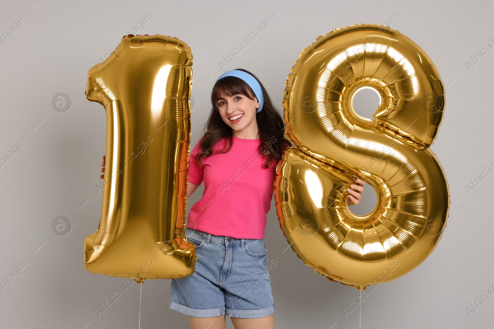 Photo of Coming of age party - 18th birthday. Young woman holding number shaped balloons on light grey background