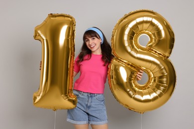 Photo of Coming of age party - 18th birthday. Young woman holding number shaped balloons on light grey background