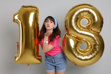 Photo of Coming of age party - 18th birthday. Young woman holding number shaped balloons on light grey background