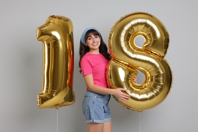 Photo of Coming of age party - 18th birthday. Young woman holding number shaped balloons on light grey background