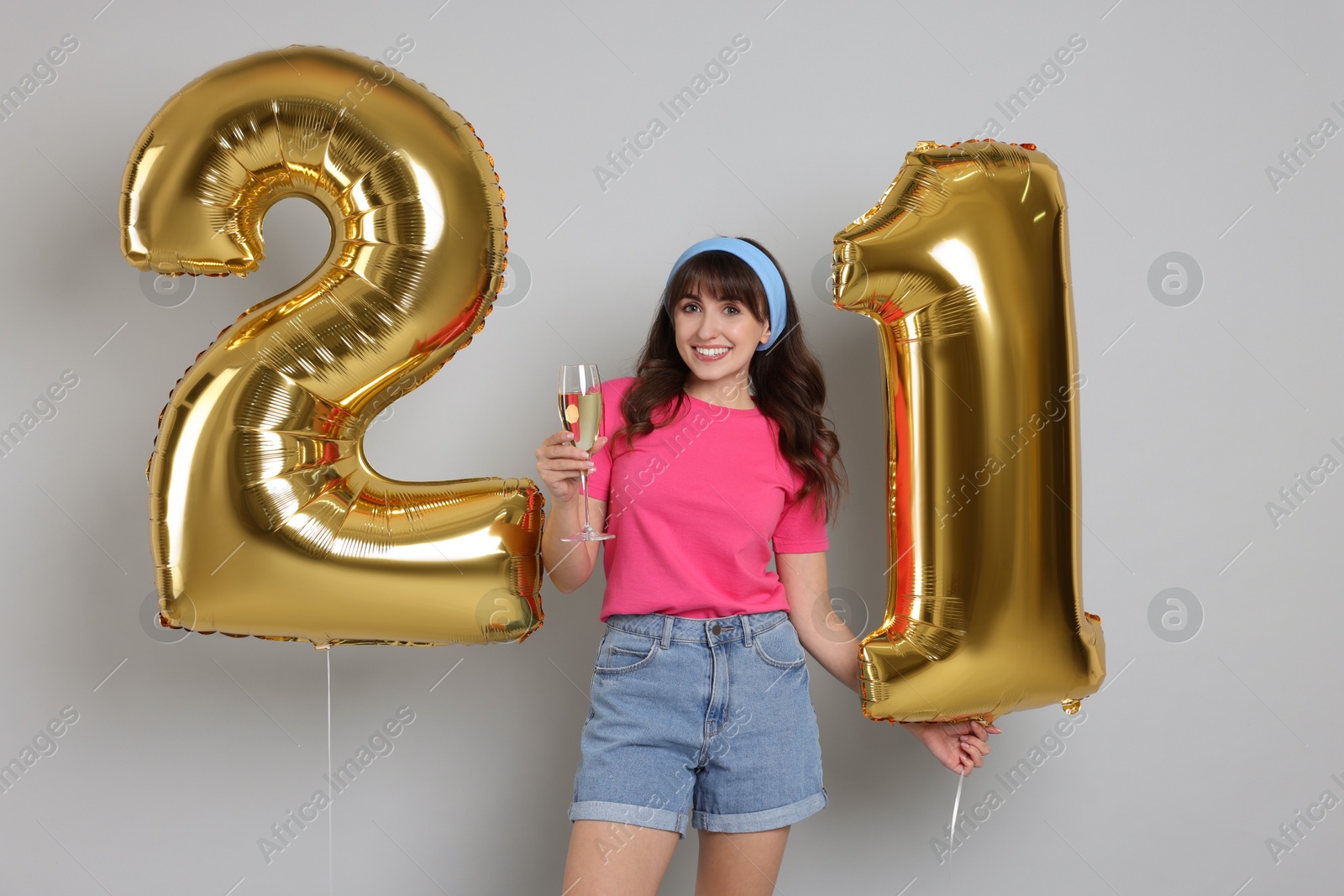 Photo of Coming of age party - 21st birthday. Young woman with glass of wine holding number shaped balloons on light grey background