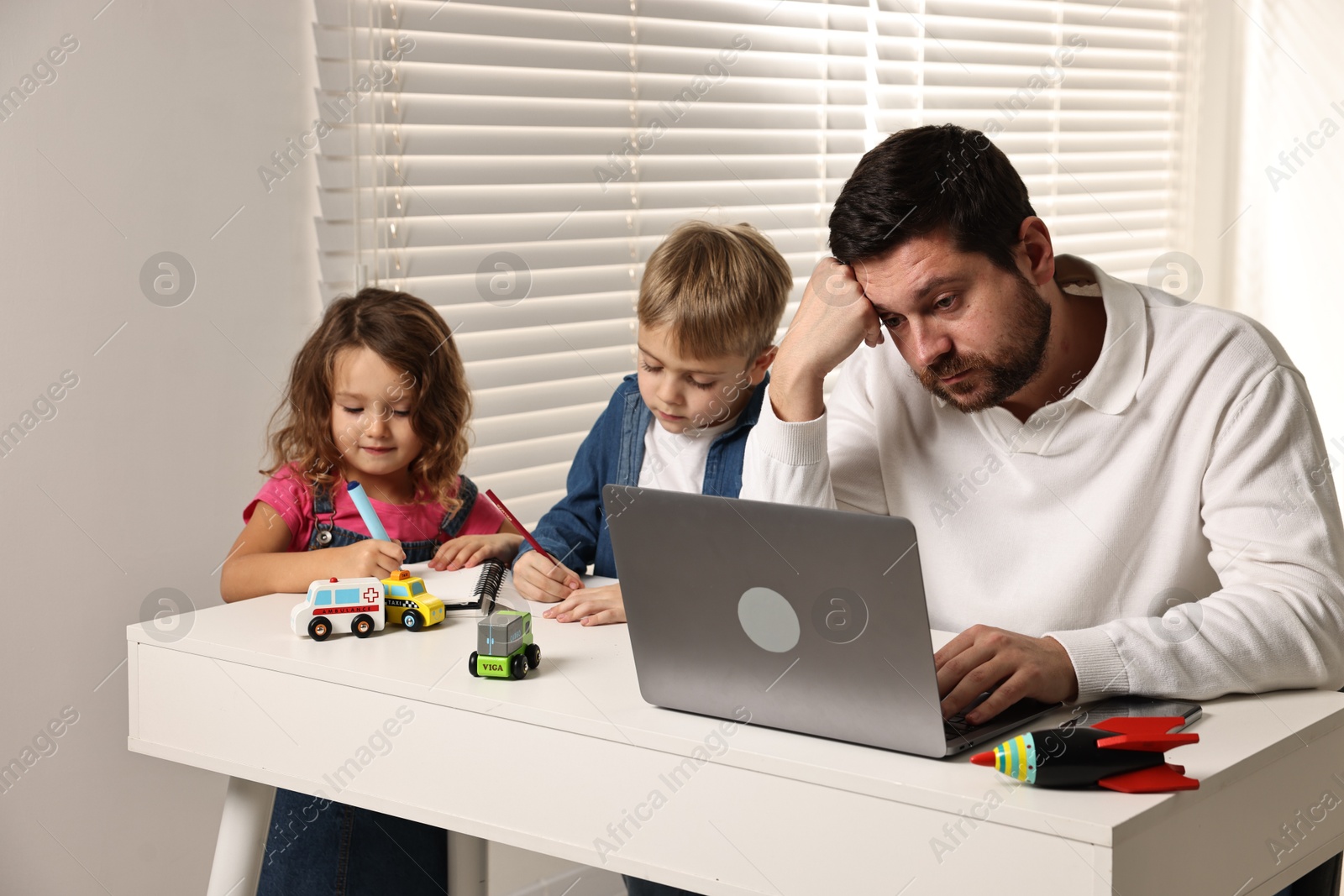 Photo of Naughty children and their overwhelmed father at table with laptop indoors