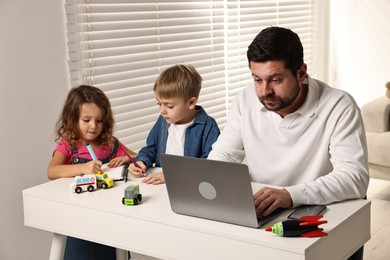 Photo of Naughty children and their overwhelmed father at table with laptop indoors