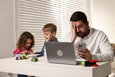 Photo of Naughty children and their overwhelmed father at table with laptop indoors