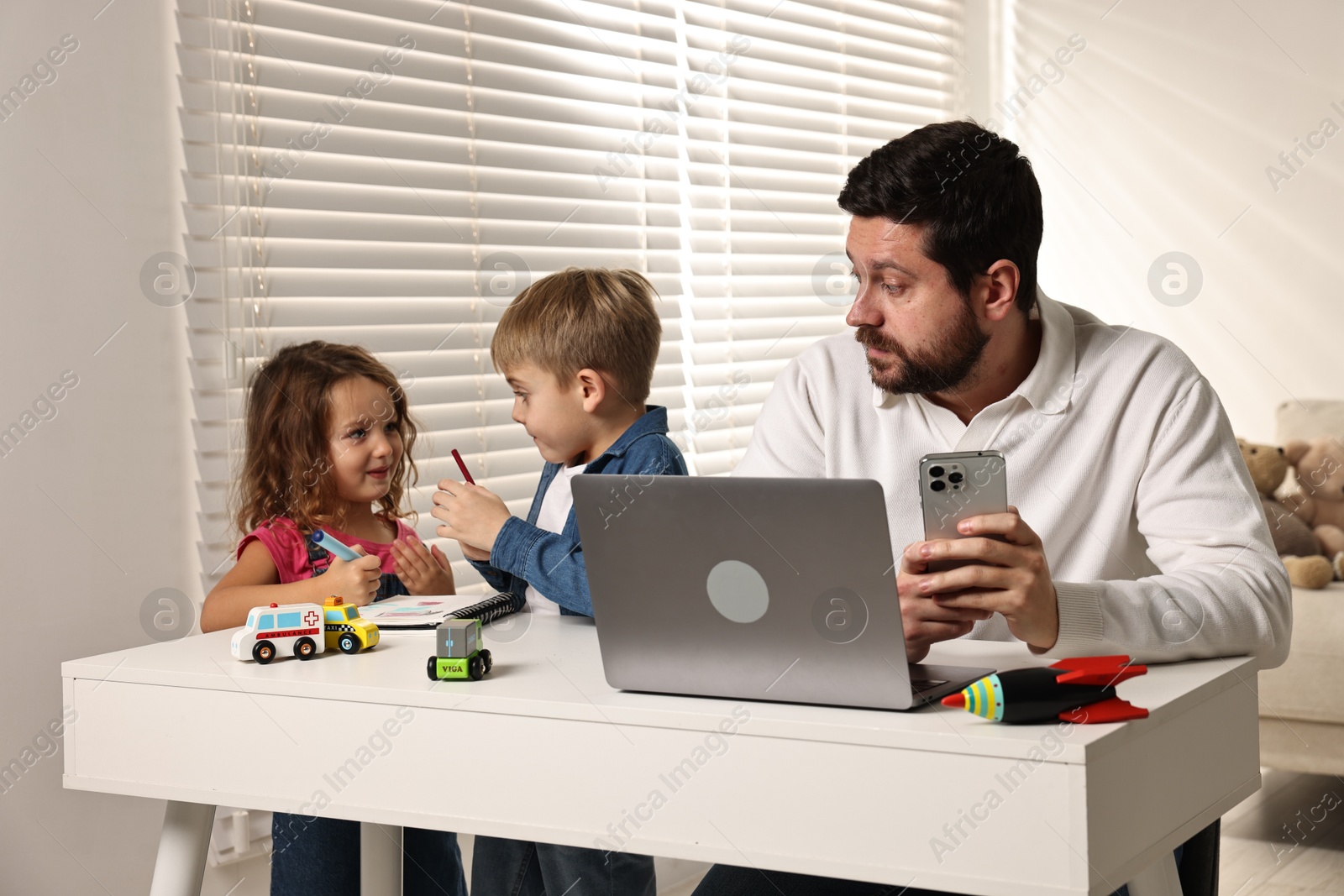 Photo of Naughty children and their overwhelmed father at table with laptop indoors