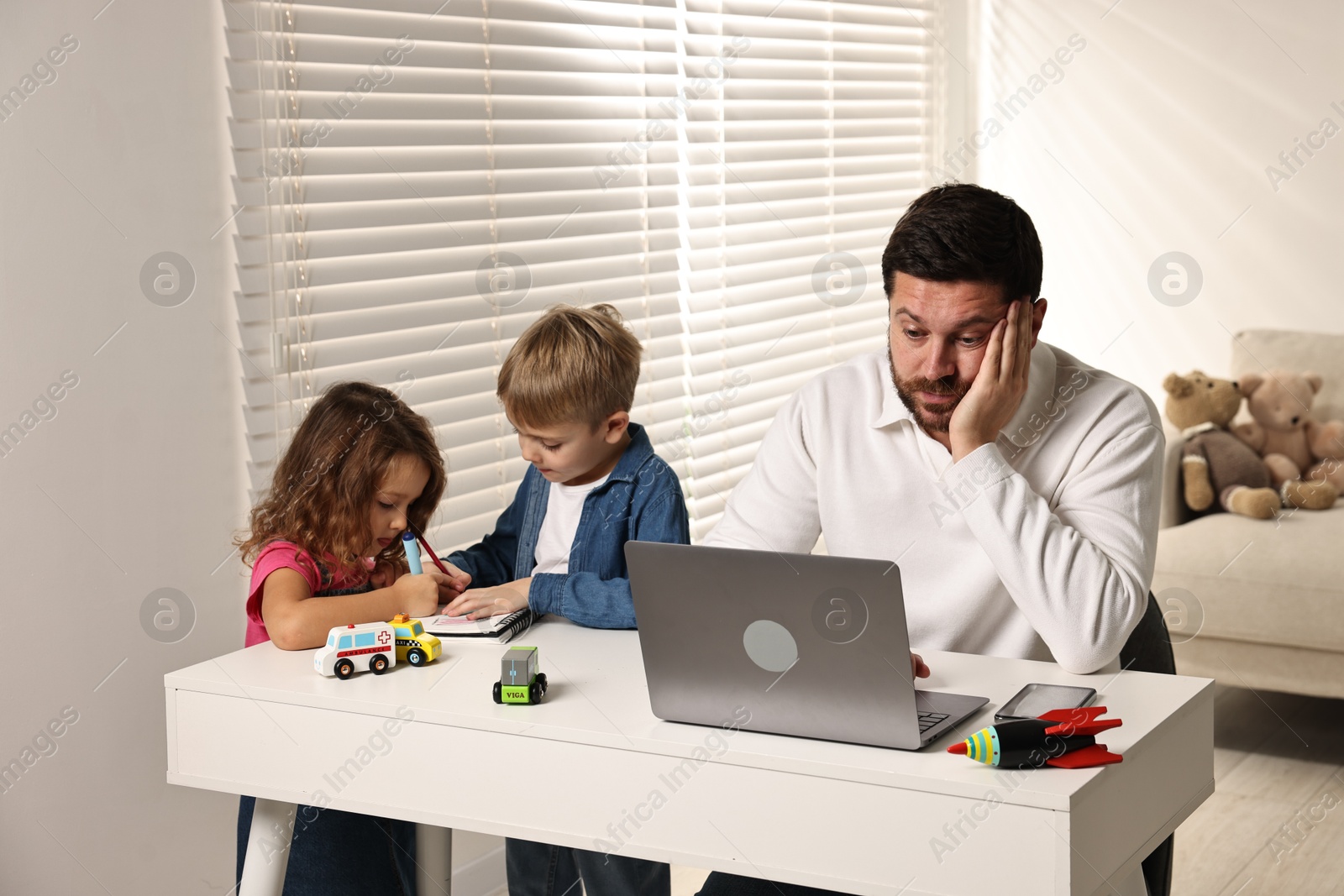 Photo of Naughty children and their overwhelmed father at table with laptop indoors