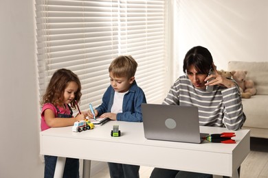 Photo of Naughty children drawing while their overwhelmed mother talking on smartphone at table indoors