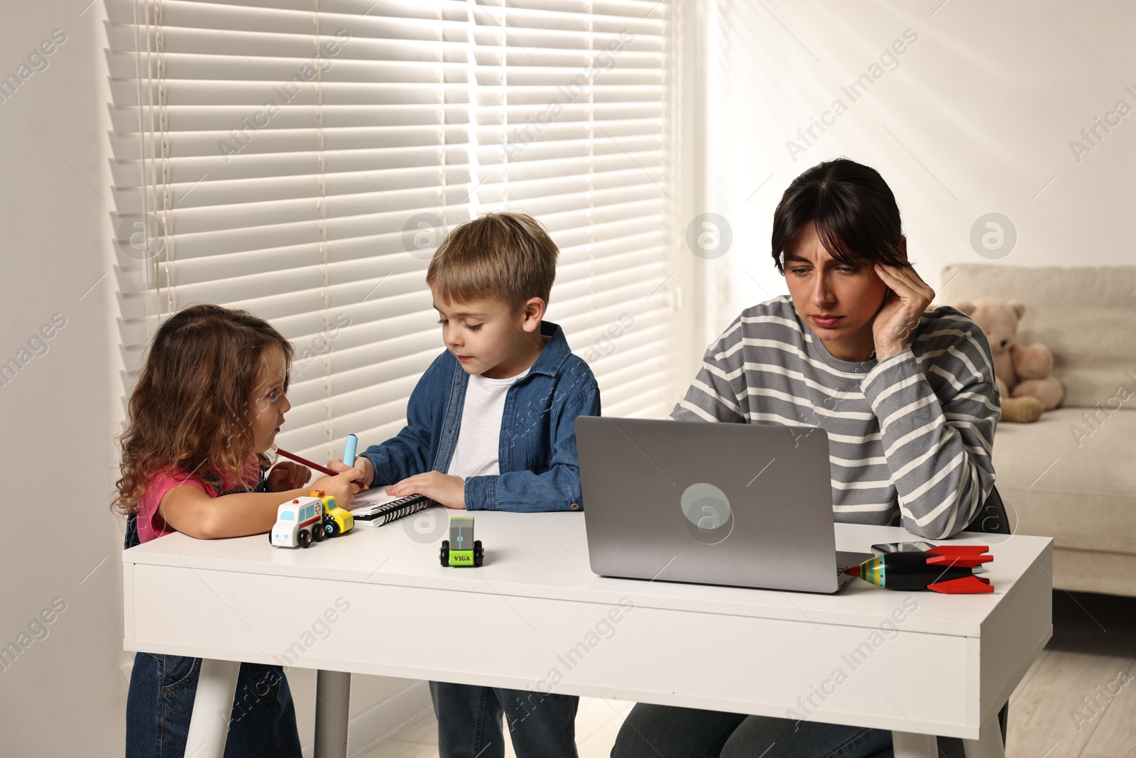 Photo of Naughty children and their overwhelmed mother at table with laptop indoors