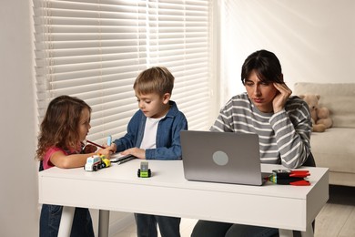 Photo of Naughty children and their overwhelmed mother at table with laptop indoors