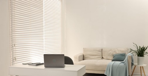 Photo of Desk with laptop, sofa and houseplant in spacious room, space for text. Interior design