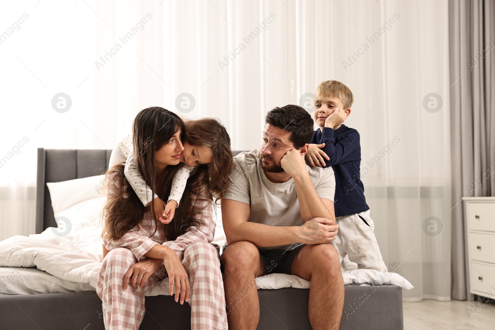 Photo of Playful children and their overwhelmed parents on bed at home