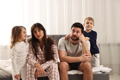 Playful children and their overwhelmed parents on bed at home