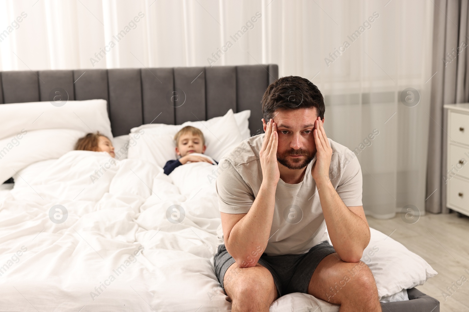 Photo of Overwhelmed father and his children on bed at home