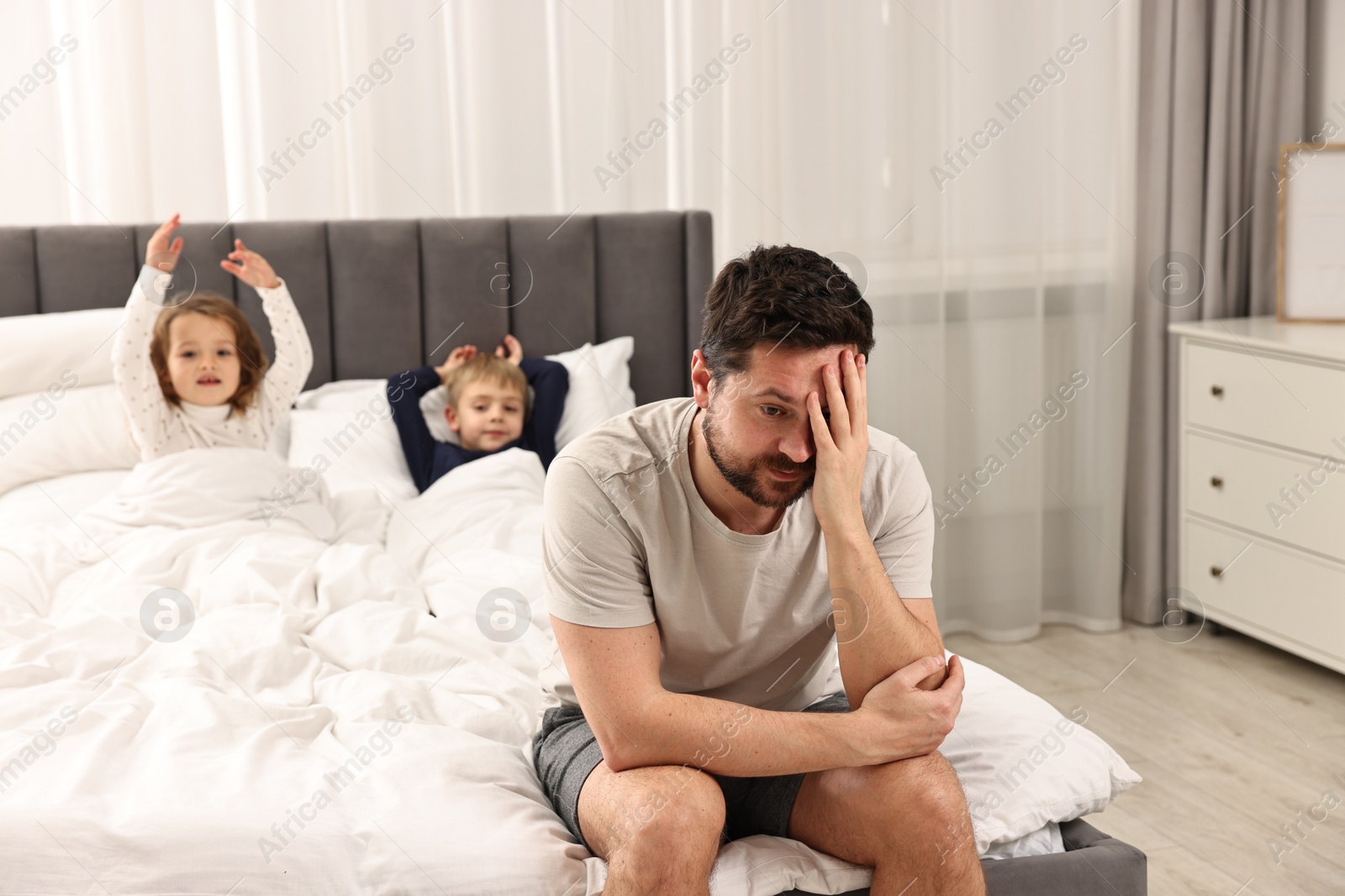 Photo of Overwhelmed father and his naughty children on bed at home