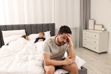 Photo of Overwhelmed father and his naughty children on bed at home