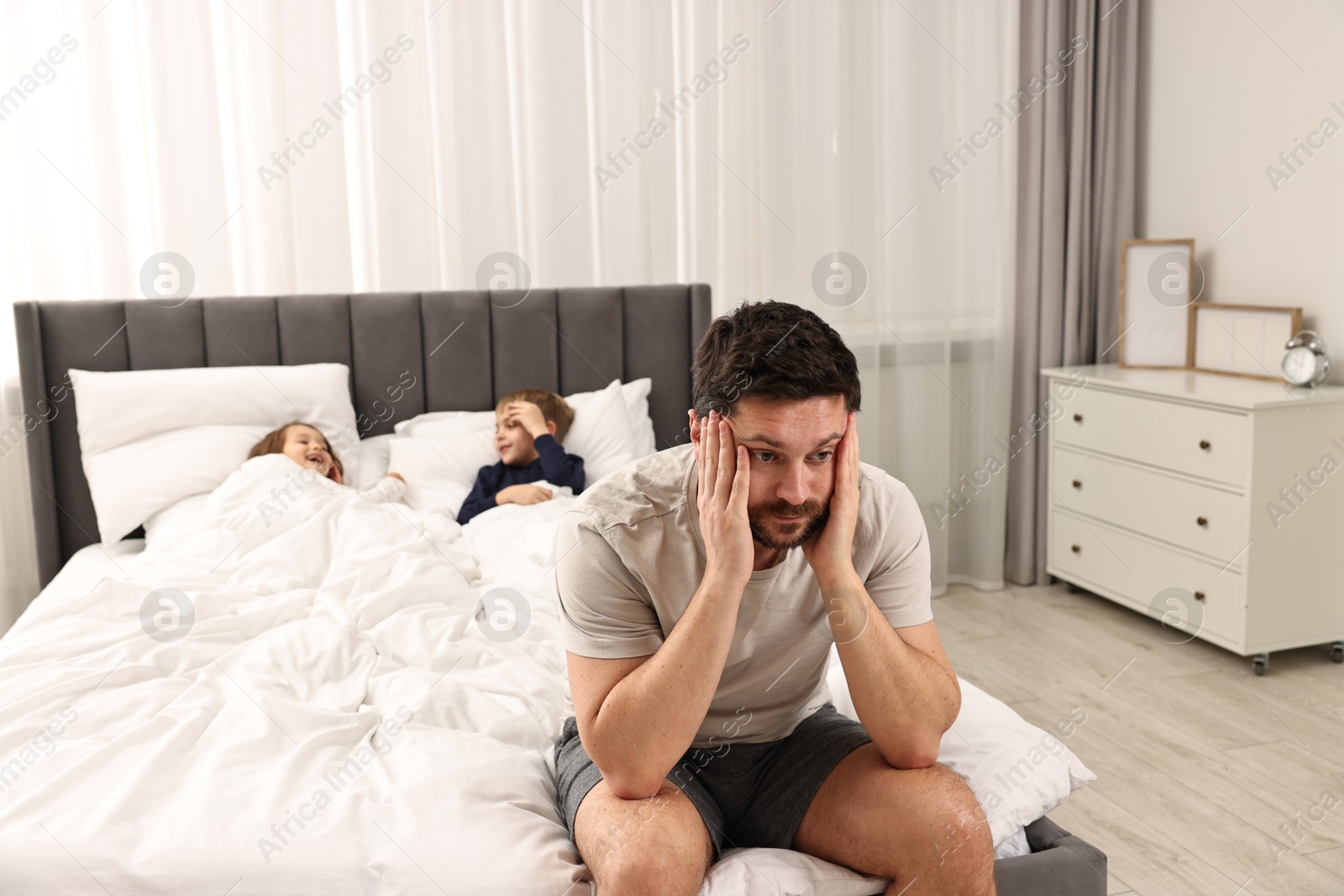 Photo of Overwhelmed father and his naughty children on bed at home