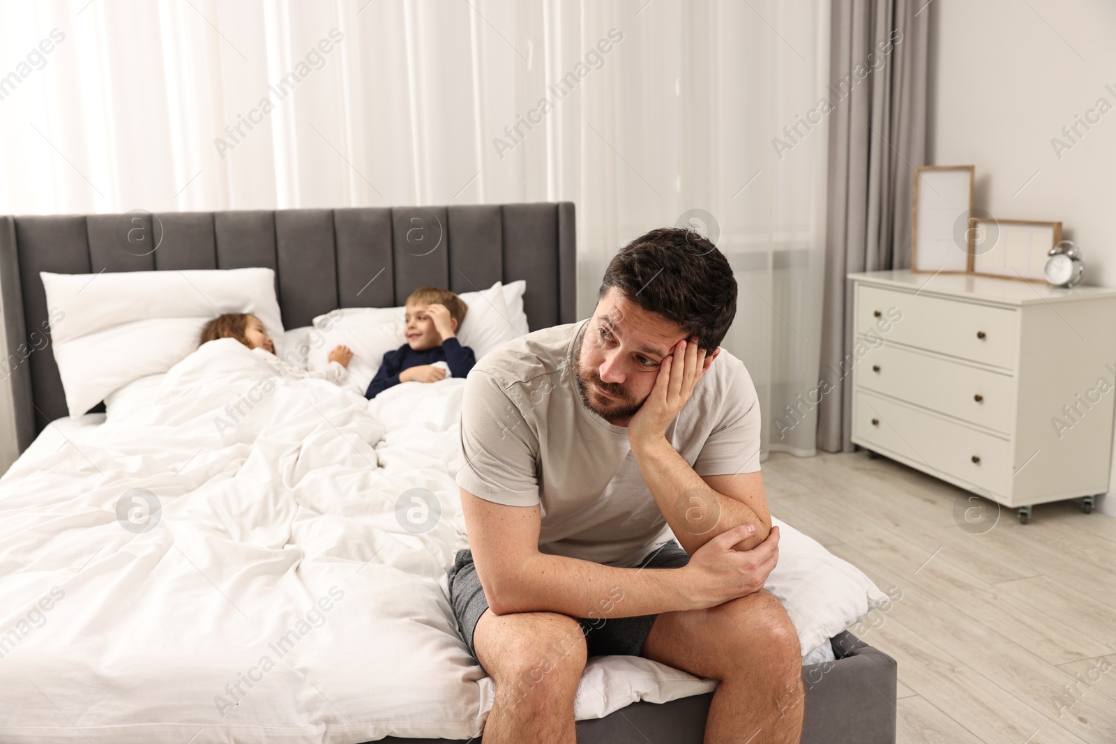 Photo of Overwhelmed father and his naughty children on bed at home