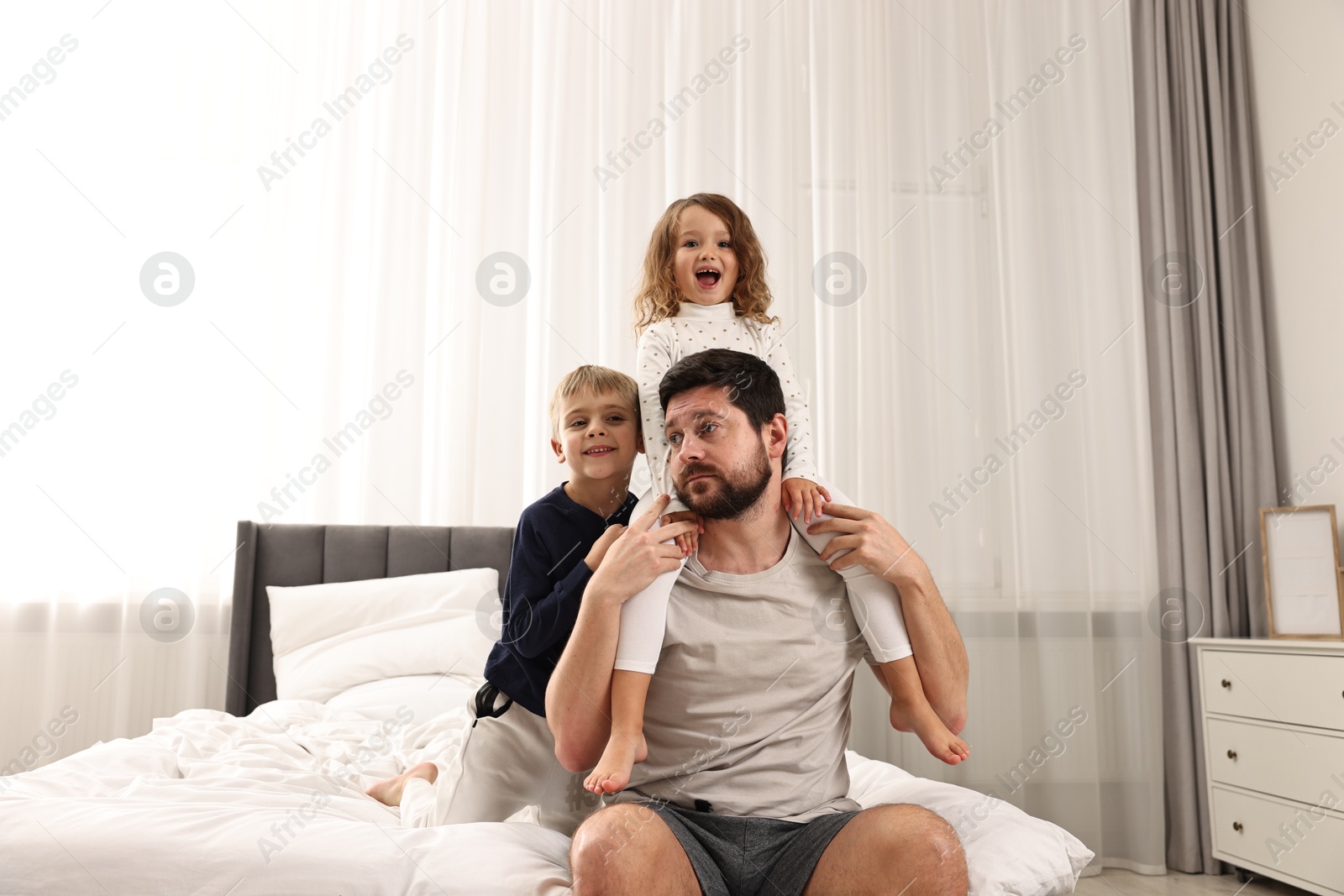 Photo of Overwhelmed father and his playful children on bed at home