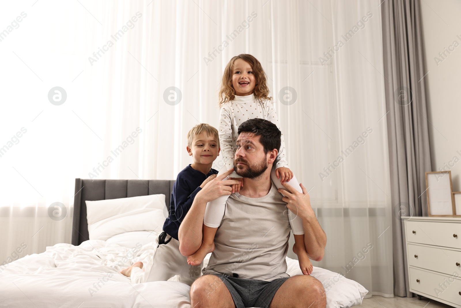 Photo of Overwhelmed father and his playful children on bed at home