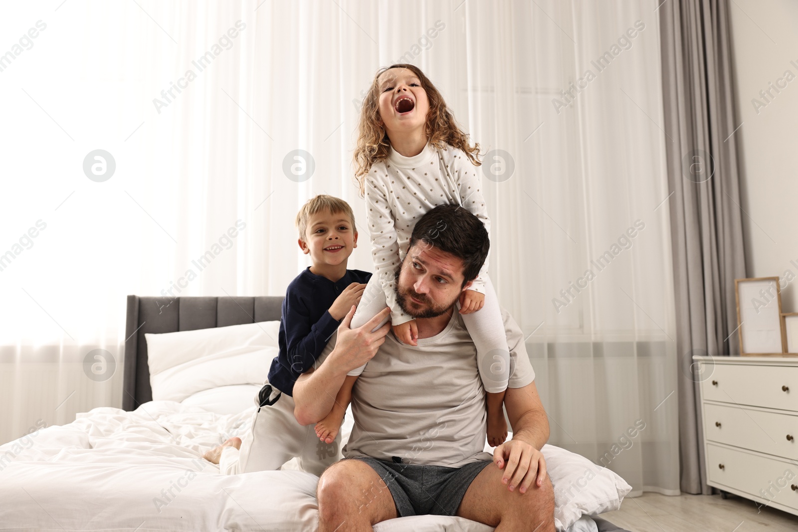 Photo of Overwhelmed father and his playful children on bed at home