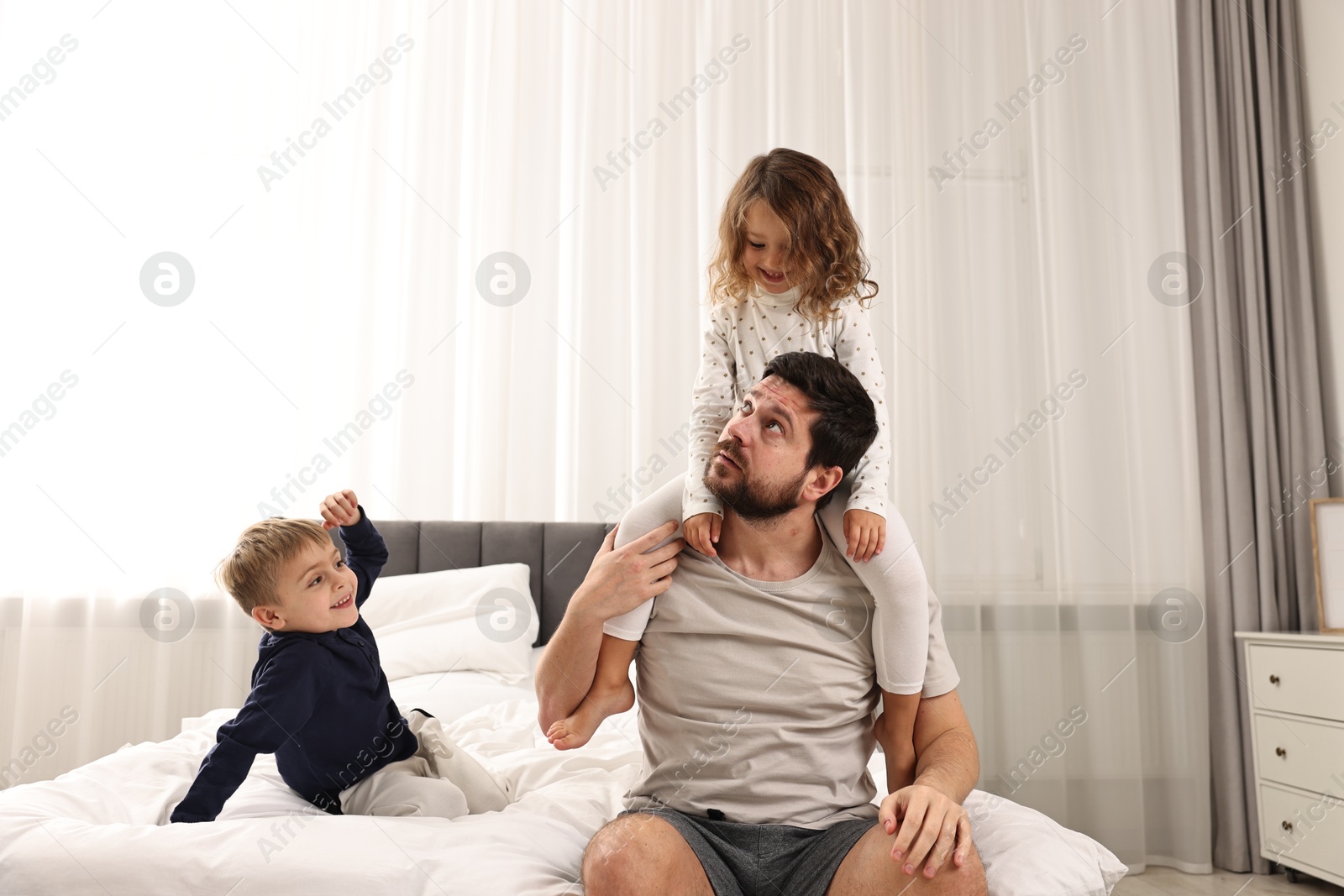 Photo of Overwhelmed father and his playful children on bed at home