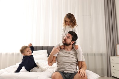 Overwhelmed father and his playful children on bed at home