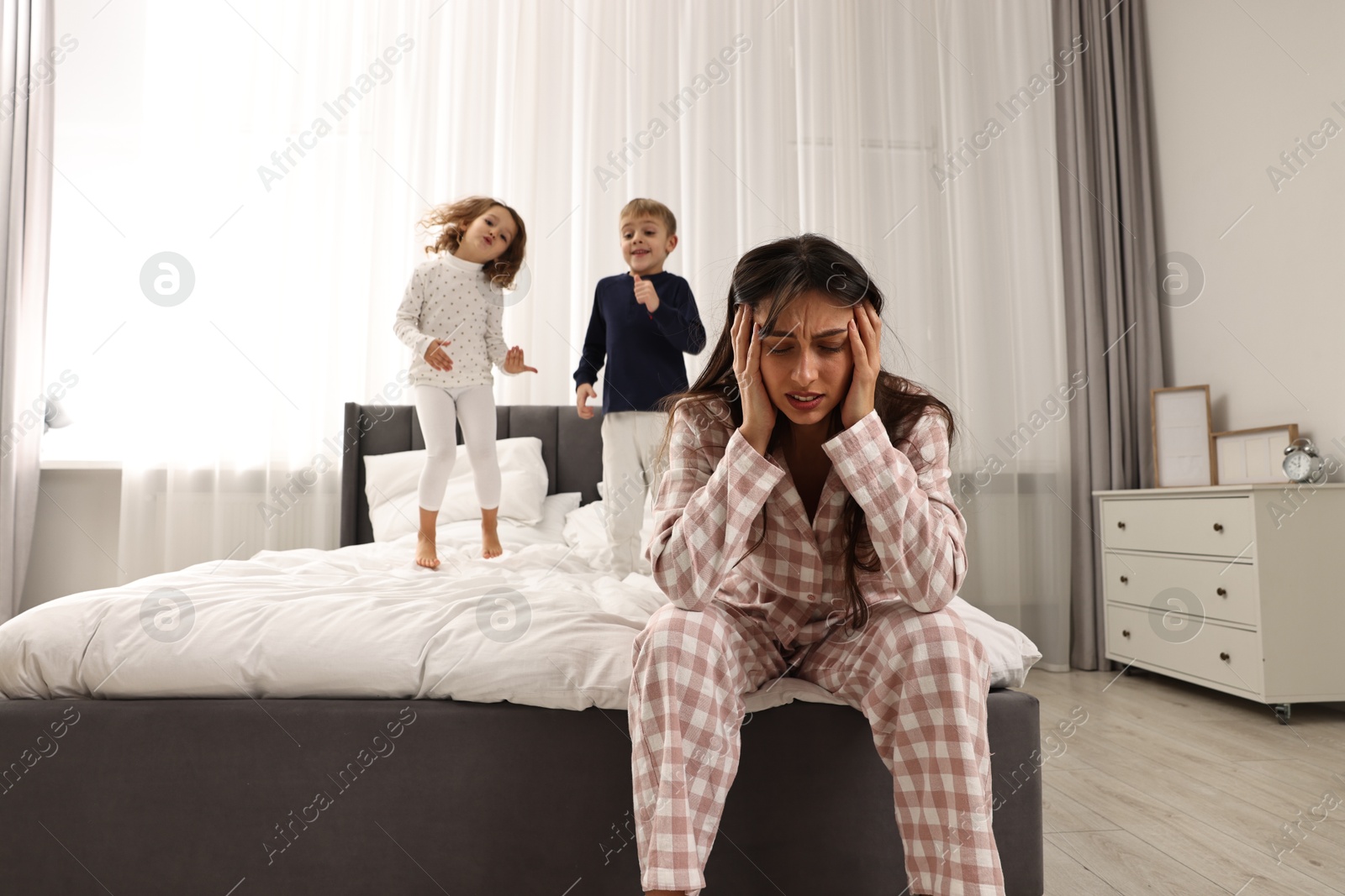 Photo of Overwhelmed mother and her playful children on bed at home