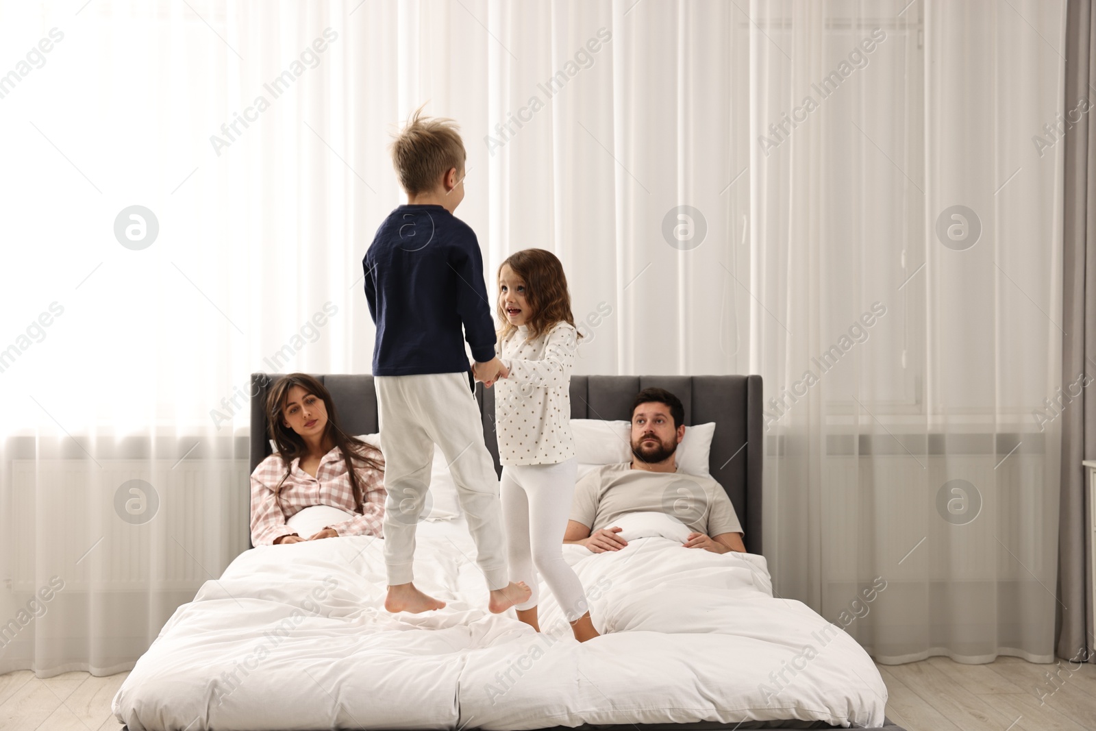 Photo of Overwhelmed parents and their playful children on bed at home