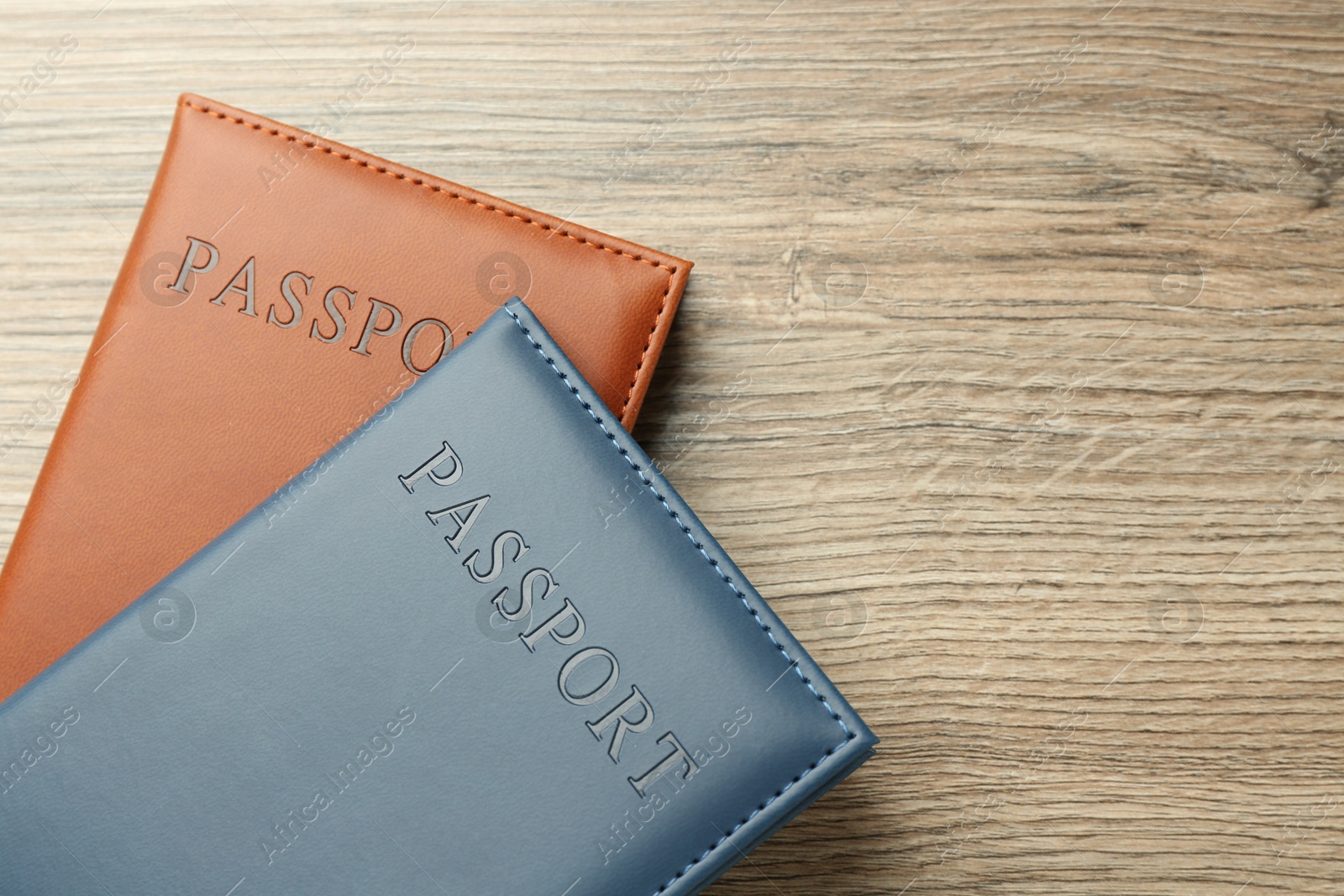 Photo of Passports in color covers on wooden table, top view. Space for text