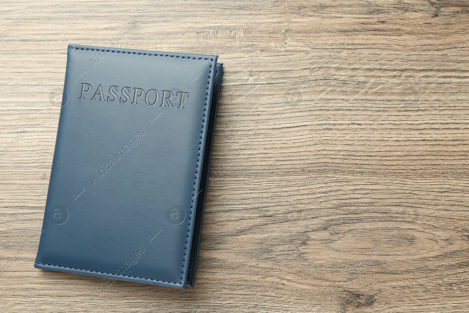 Photo of Passport in blue cover on wooden table, top view. Space for text