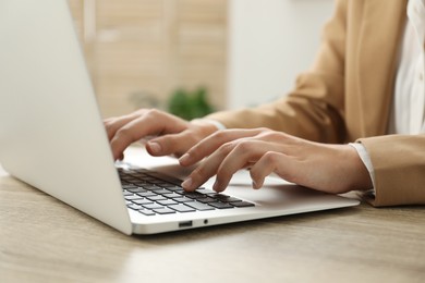 Photo of Businesswoman using laptop at wooden table indoors, closeup. Modern technology