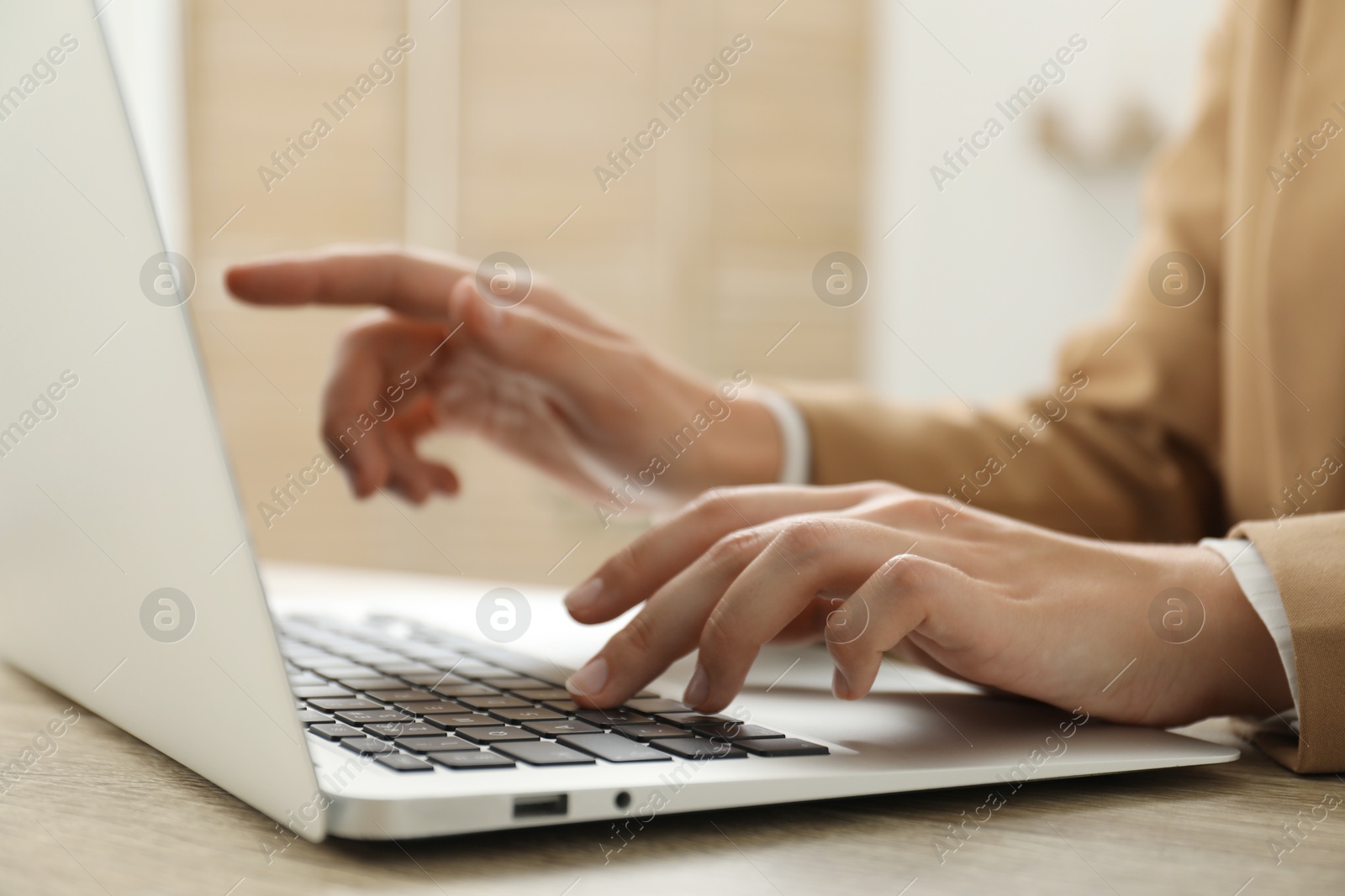 Photo of Businesswoman using laptop at wooden table indoors, closeup. Modern technology