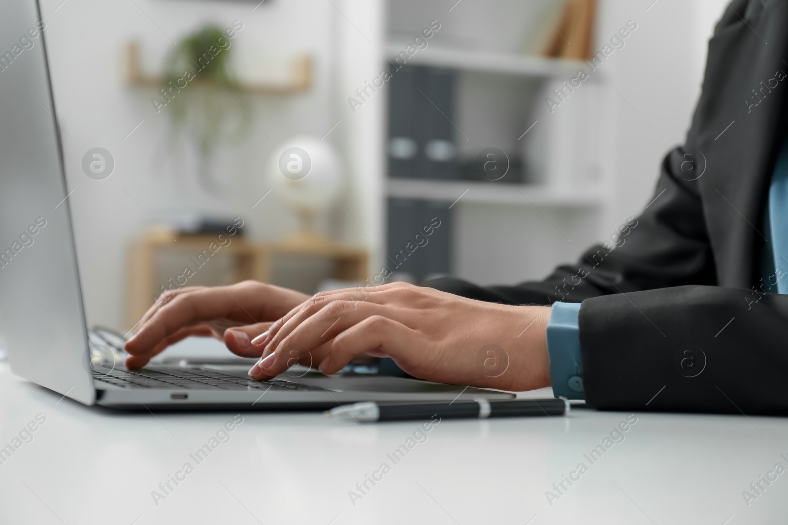 Photo of Businesswoman using laptop at white table indoors, closeup. Modern technology